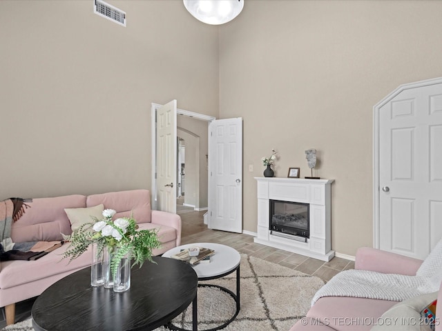 living room with a glass covered fireplace, visible vents, a high ceiling, wood tiled floor, and baseboards