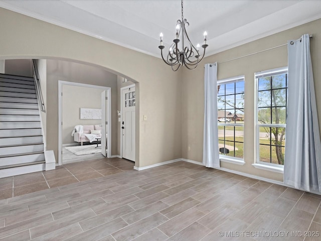 unfurnished dining area with arched walkways, crown molding, a notable chandelier, and stairway