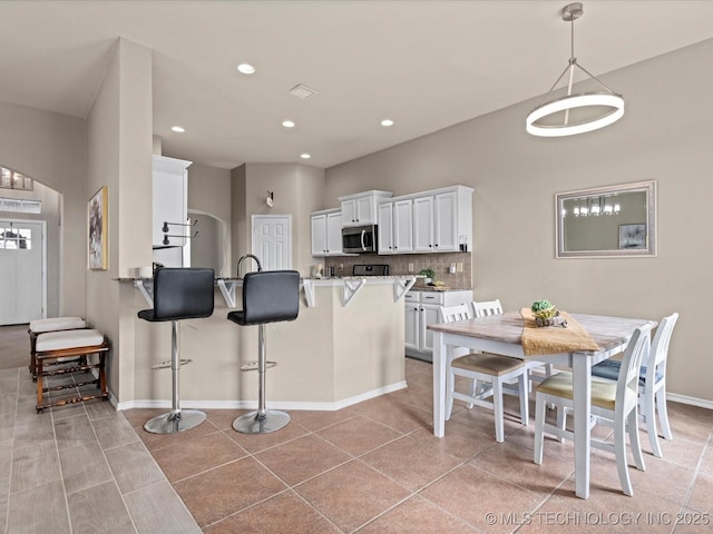 kitchen with a kitchen breakfast bar, a peninsula, stainless steel microwave, white cabinetry, and backsplash