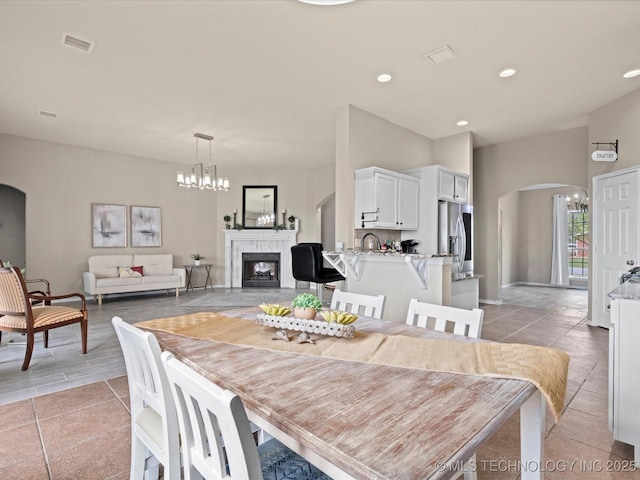 dining space featuring visible vents, arched walkways, a chandelier, and a tile fireplace