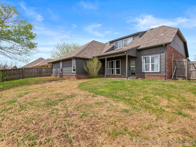 rear view of property featuring brick siding, a fenced backyard, a lawn, and roof with shingles