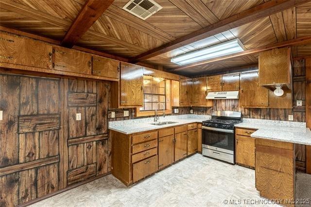 703 N Sioux Ave, Claremore, OK 74017 - kitchen with stainless steel gas range oven, under cabinet range hood, brown cabinetry, wooden walls, and light countertops