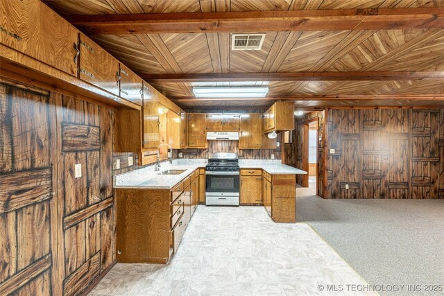 703 N Sioux Ave, Claremore, OK 74017 - kitchen with stainless steel range with gas cooktop, brown cabinets, wooden walls, under cabinet range hood, and light countertops