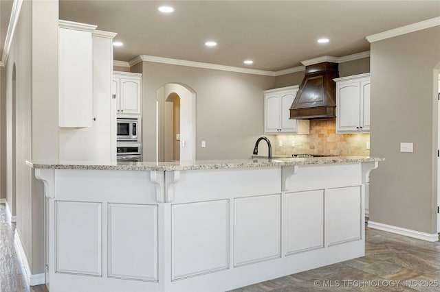 kitchen featuring recessed lighting, arched walkways, light stone counters, stainless steel appliances, and white cabinets