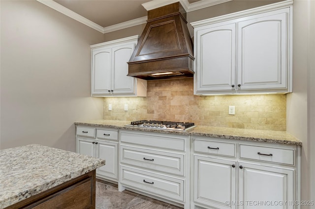 kitchen featuring white cabinetry, crown molding, light stone countertops, custom exhaust hood, and stainless steel gas cooktop