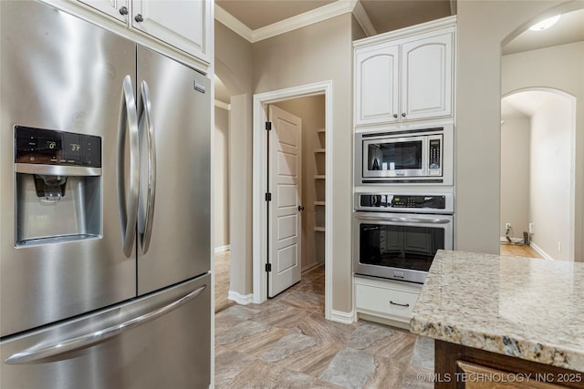 kitchen with light stone countertops, arched walkways, stainless steel appliances, white cabinets, and ornamental molding