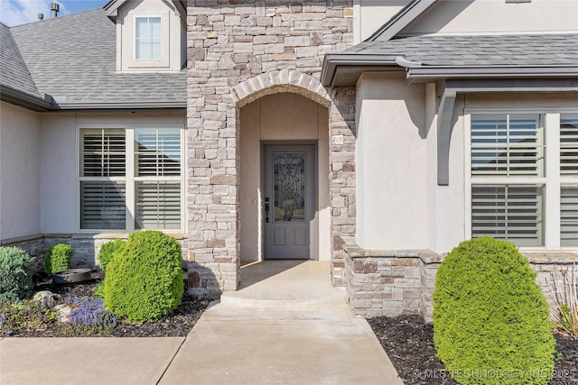 property entrance with roof with shingles, stucco siding, and stone siding