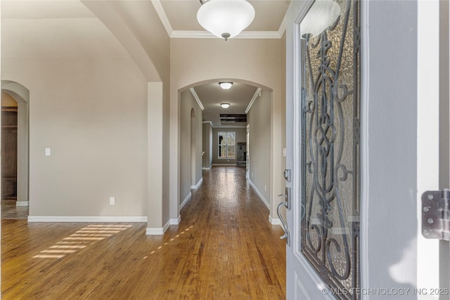 corridor featuring wood finished floors, baseboards, ornamental molding, and arched walkways