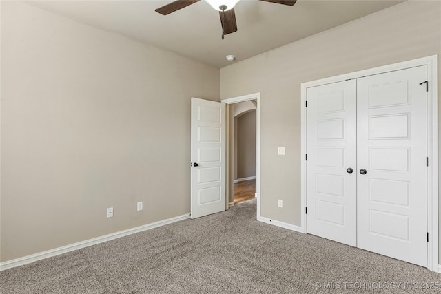 unfurnished bedroom featuring carpet flooring, ceiling fan, baseboards, arched walkways, and a closet