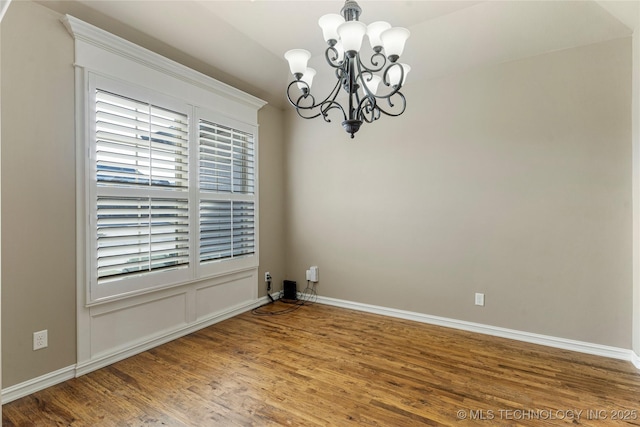 spare room with a chandelier, baseboards, and wood finished floors