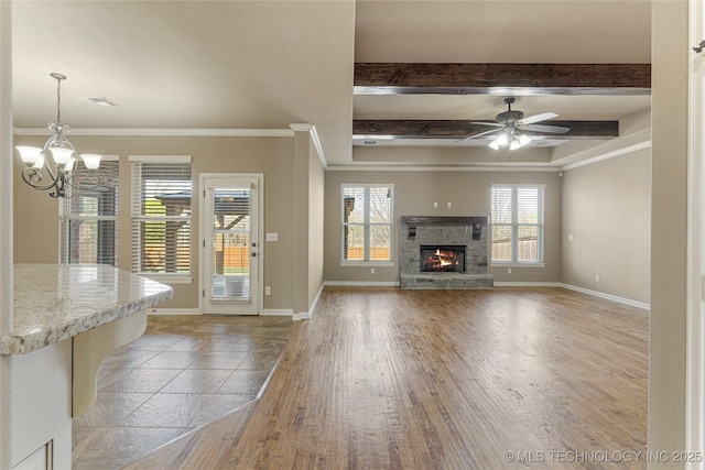 unfurnished living room featuring light wood-style floors, ornamental molding, ceiling fan with notable chandelier, a stone fireplace, and baseboards