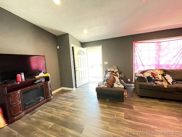 living room featuring a textured ceiling, baseboards, vaulted ceiling, and wood finished floors