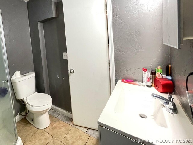 bathroom with vanity, toilet, a textured wall, tile patterned floors, and a stall shower