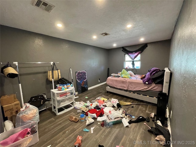 bedroom featuring baseboards, visible vents, wood finished floors, and a textured ceiling