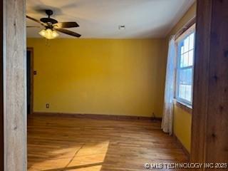 unfurnished room with baseboards, wood finished floors, and a ceiling fan