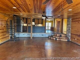 interior space featuring a ceiling fan, concrete flooring, wooden ceiling, and wooden walls