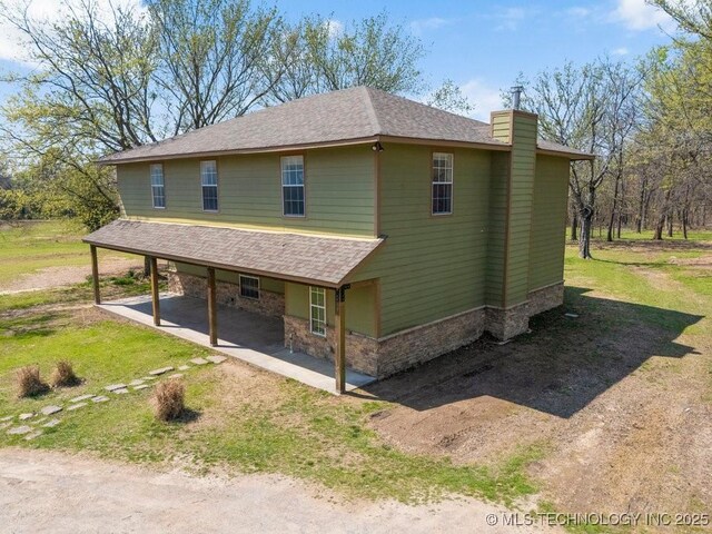 9012 S 49th W Ave, Tulsa, OK 74131 - view of side of home with a patio, roof with shingles, stone siding, a chimney, and driveway