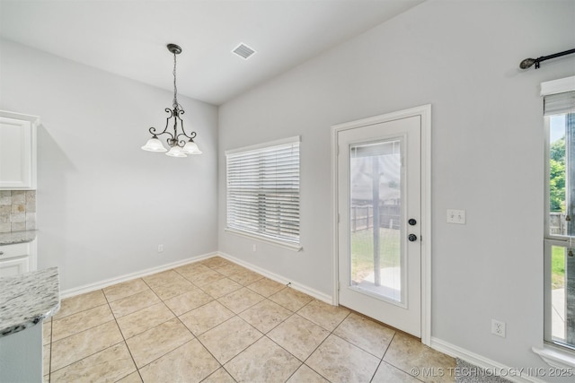 unfurnished dining area featuring a chandelier, light tile patterned flooring, and baseboards