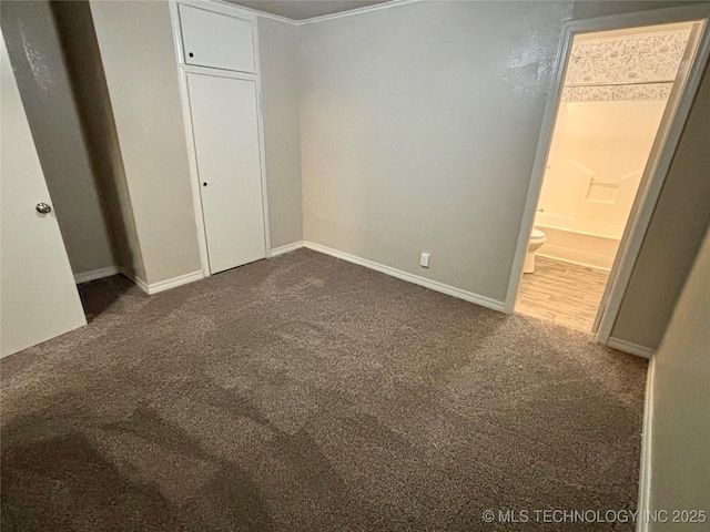 unfurnished bedroom featuring dark colored carpet, baseboards, and connected bathroom