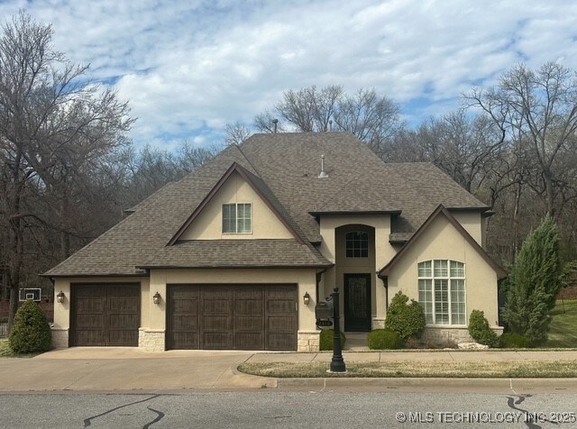 7415 E 109th St S, Tulsa, OK 74133 - french country inspired facade with a garage, concrete driveway, stucco siding, and roof with shingles