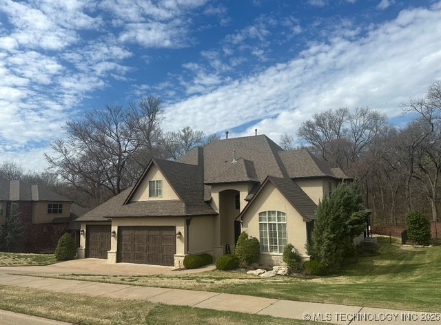 7415 E 109th St S, Tulsa, OK 74133 - french provincial home featuring driveway, a front yard, roof with shingles, stucco siding, and a garage