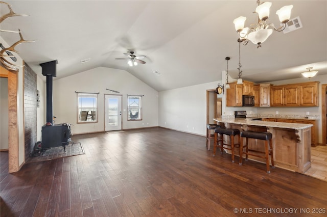kitchen with dark wood-type flooring, black microwave, ceiling fan with notable chandelier, a wood stove, and electric range