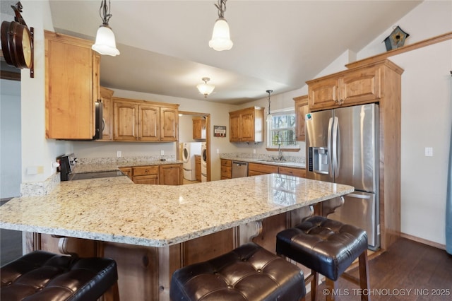 kitchen with washing machine and clothes dryer, a peninsula, appliances with stainless steel finishes, and a kitchen bar