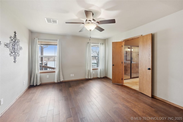 unfurnished bedroom featuring multiple windows, visible vents, wood finished floors, and baseboards