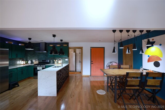 kitchen with decorative backsplash, wall chimney exhaust hood, appliances with stainless steel finishes, a sink, and green cabinetry