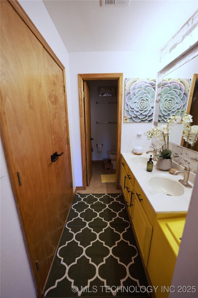 full bathroom with double vanity, toilet, a sink, and a textured ceiling