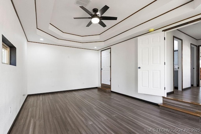unfurnished room featuring a tray ceiling, baseboards, visible vents, a ceiling fan, and wood finished floors