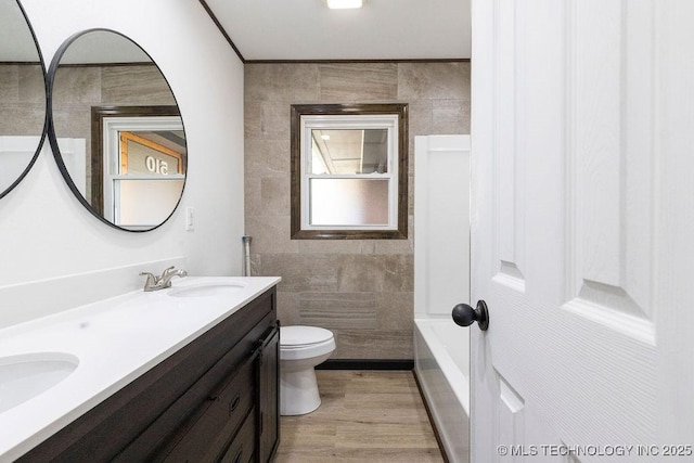 full bathroom featuring tile walls, double vanity, toilet, wood finished floors, and a sink