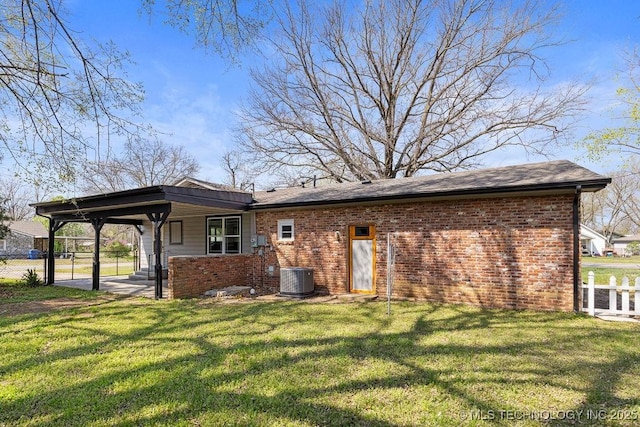 rear view of house featuring brick siding, a carport, fence, and a lawn