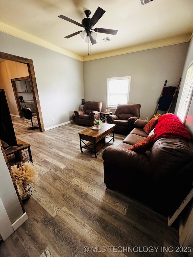 living area featuring crown molding, baseboards, ceiling fan, and wood finished floors
