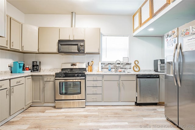 kitchen with a sink, cream cabinets, stainless steel appliances, and light wood-type flooring