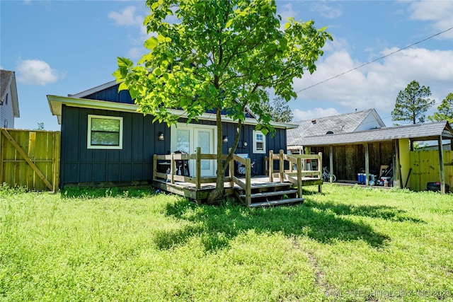 back of property with fence, a wooden deck, board and batten siding, and a yard