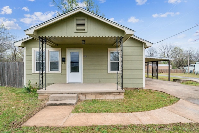 bungalow-style home with fence, a front yard, an attached carport, driveway, and a porch