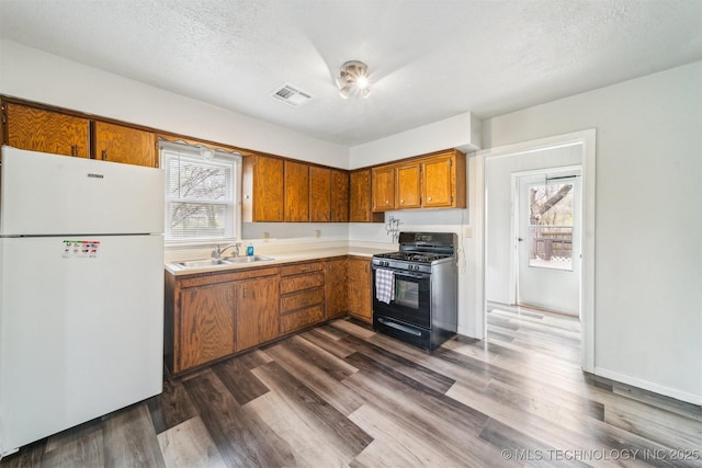 kitchen with light countertops, visible vents, a sink, black gas range, and freestanding refrigerator