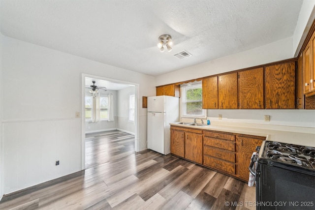 kitchen with plenty of natural light, black range with gas stovetop, wood finished floors, brown cabinetry, and freestanding refrigerator