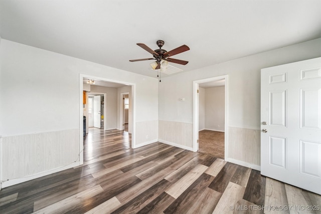 empty room with a wainscoted wall, wood finished floors, and a ceiling fan
