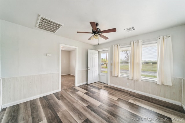 empty room featuring a wainscoted wall, visible vents, wood finished floors, and a ceiling fan