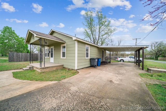 view of side of property with an attached carport, concrete driveway, fence, and a lawn