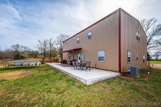 rear view of house with central air condition unit, a yard, a patio, and a trampoline