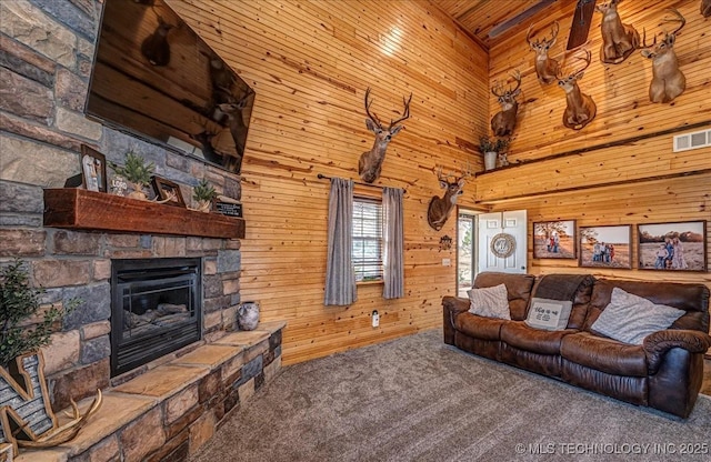 carpeted living area featuring a stone fireplace, visible vents, a high ceiling, and wood walls