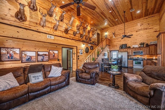 living area with visible vents, wood walls, ceiling fan, a towering ceiling, and wood ceiling
