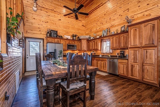 dining room with a high ceiling, wood walls, ceiling fan, and dark wood-type flooring