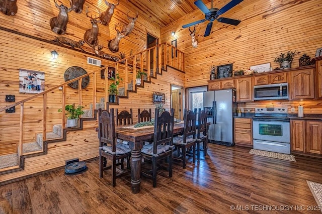dining space featuring dark wood-type flooring, stairs, ceiling fan, and wood walls