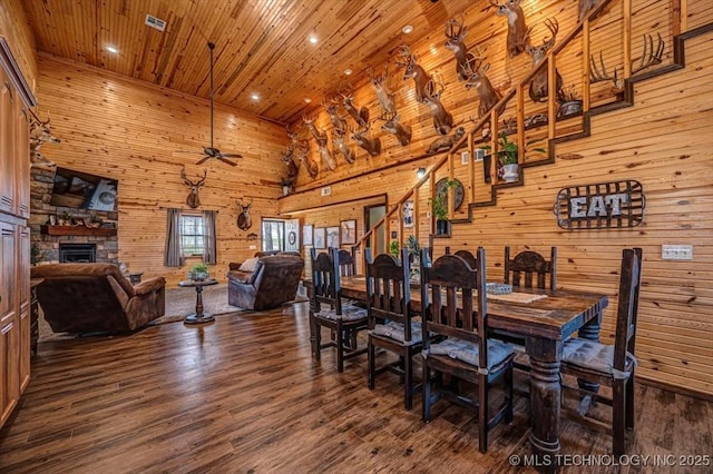 dining area featuring wood walls, a fireplace, wood finished floors, a ceiling fan, and wooden ceiling