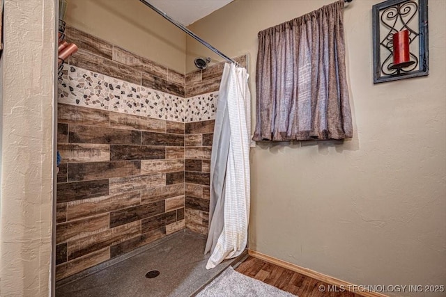 full bath with baseboards, a tile shower, and wood finished floors