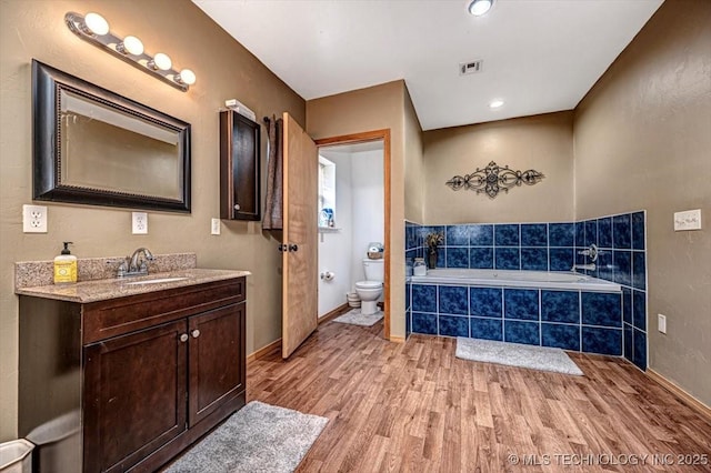 full bath with toilet, vanity, a garden tub, wood finished floors, and visible vents